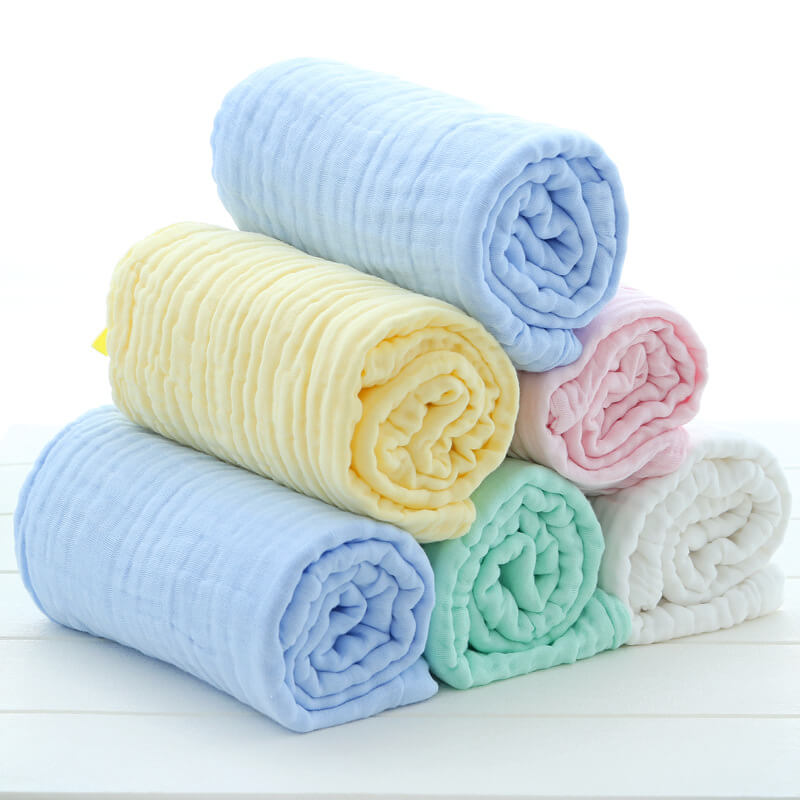 A stack of rolled 6-layer cotton muslin blankets in various solid colors including blue, yellow, mint, pink, and white.