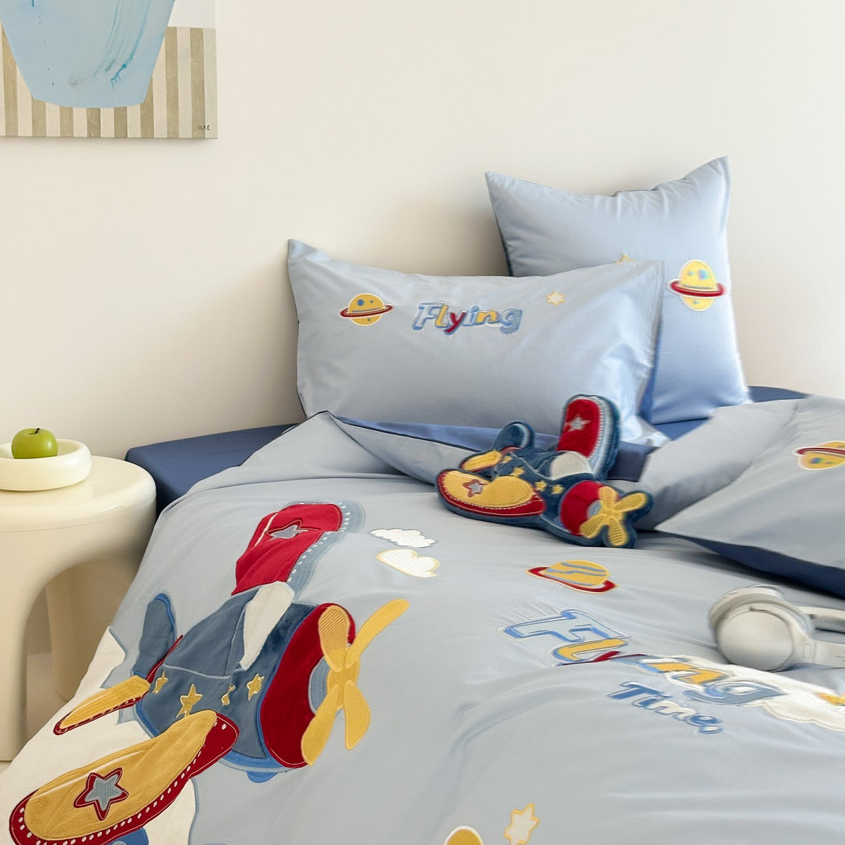 Children's bed with blue bedding featuring airplane designs and colorful text.