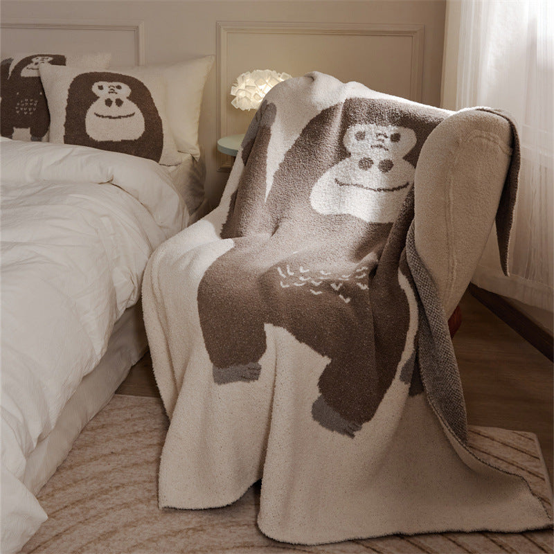 A beige and brown chimpanzee soft fleece throw blanket with a face design draped over an armchair in a cozy bedroom setting.
