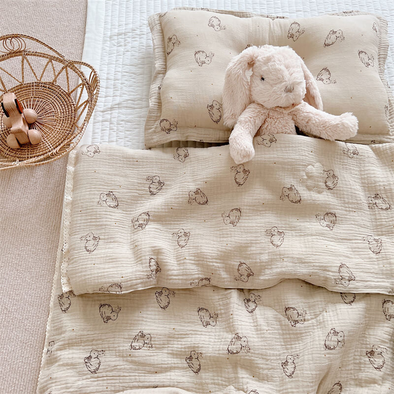 Stuffed bunny toy tucked under a beige cotton muslin comforter with brown bunny print