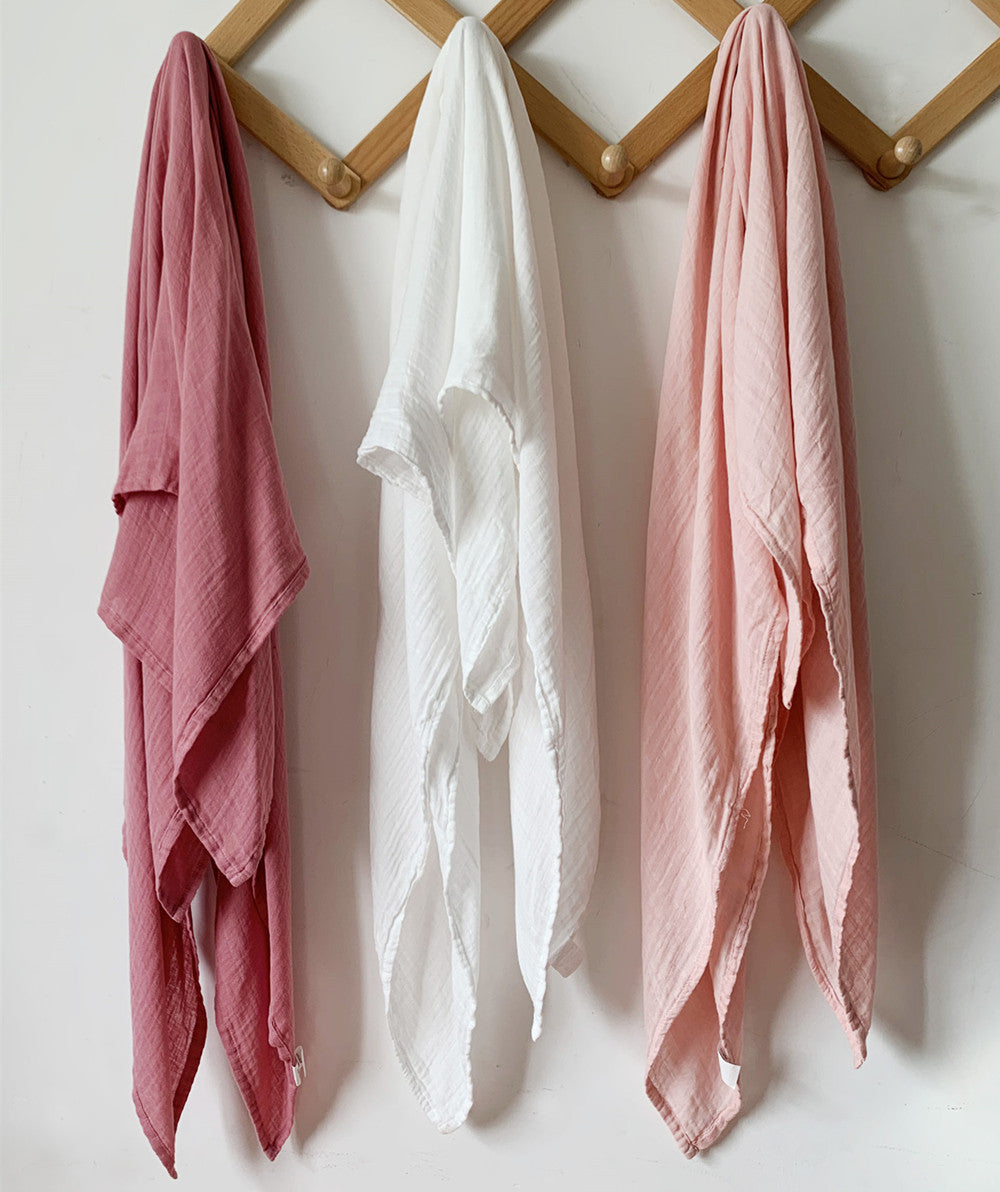Close-up of three bamboo muslin swaddle blankets showing the lightweight, crinkle texture in dusty rose, off-white, and blush pink