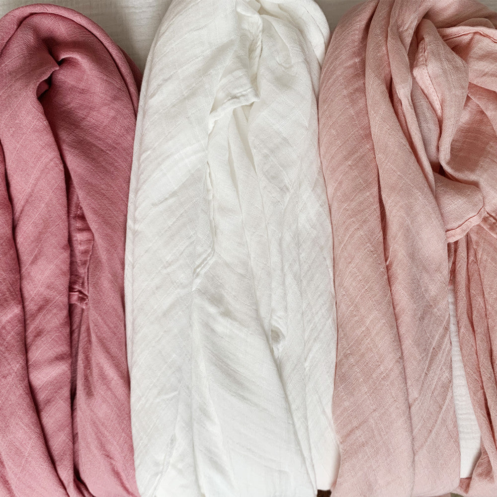 Top-down view of the soft and breathable bamboo muslin fabric texture from the 3-pack swaddle blankets in coordinating shades of pink and off-white