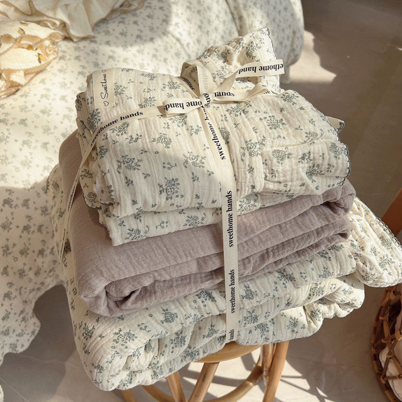 Folded green floral bedding set in cotton muslin on wooden stool