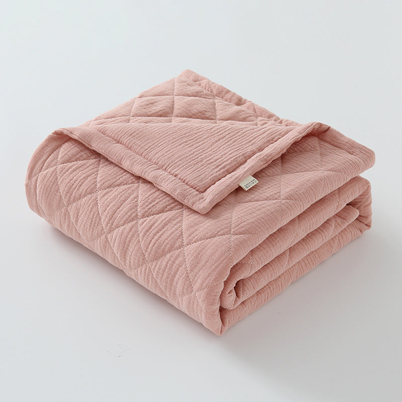 Mauve pink cotton muslin baby quilt folded with fine stitching and gentle tones