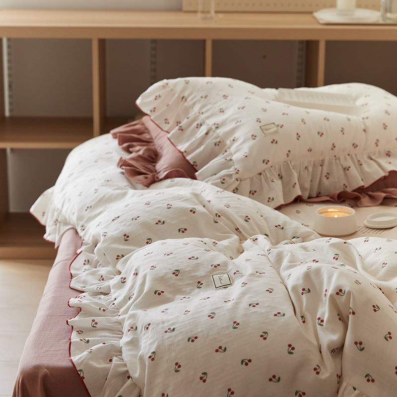 The cherry-print cotton muslin bedding set with ruffle trim, draped on a bed in a bright room, creating a cozy and relaxed atmosphere.