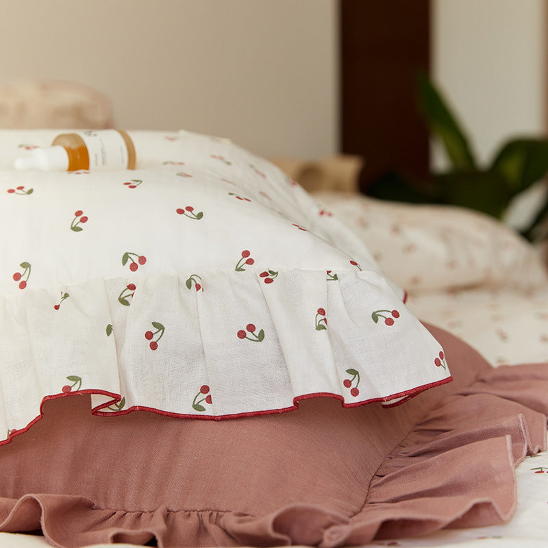 The corner of a cherry-print cotton muslin pillowcase, showing the soft, textured material and the subtle ruffle detail.