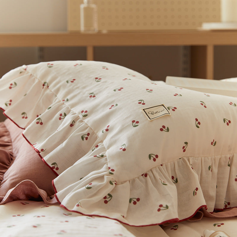 The full bedding set, including the duvet cover and pillowcases, spread out on a white surface, highlighting the vibrant cherry print and ruffle design.
