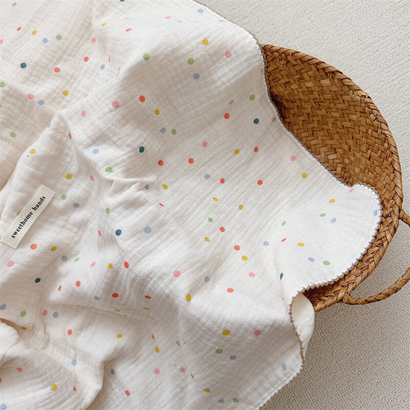 A close-up of the Colorful Dot muslin blanket, 47"x51", draped over a woven basket, highlighting its soft, crinkled texture and the playful assortment of multi-colored polka dots.