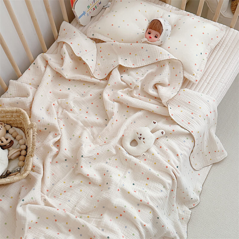 The Colorful Dot muslin blanket and pillow set styled in a crib with a doll and a plush toy, creating a vibrant and cheerful nursery scene.