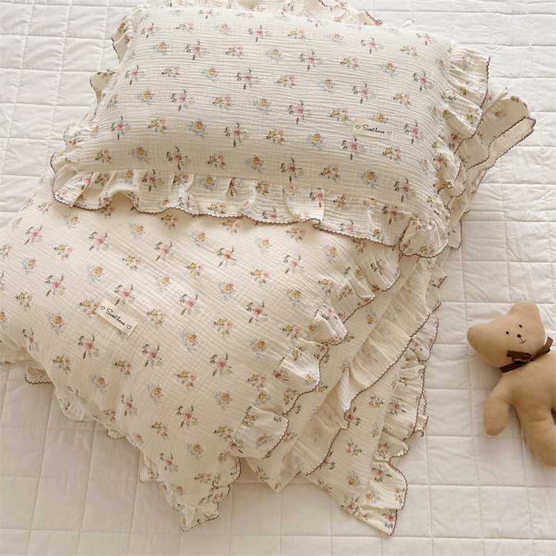 Floral-patterned pillow with ruffles on a textured surface next to a teddy bear.