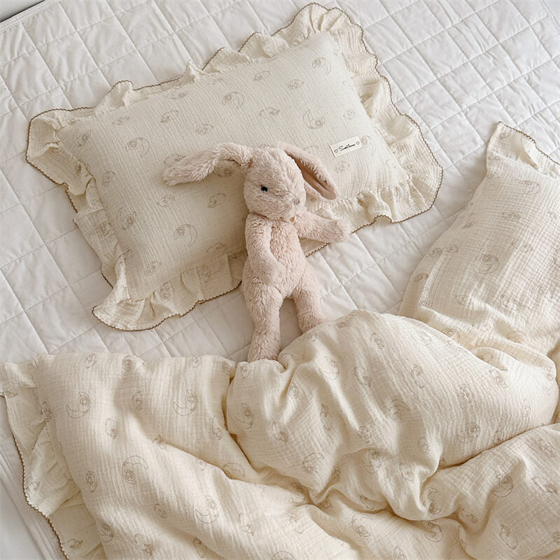 Soft cotton muslin pillow with ruffle edge and subtle lamb print, paired with plush bunny toy on white quilt