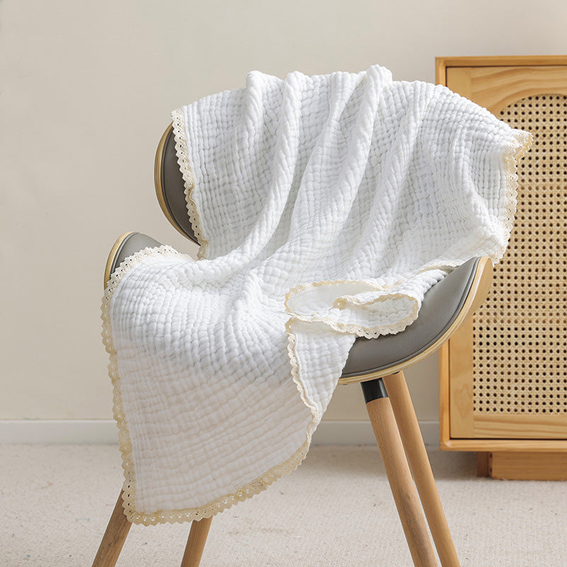 A white 6-layer muslin baby blanket with delicate lace trim draped over a gray chair.
