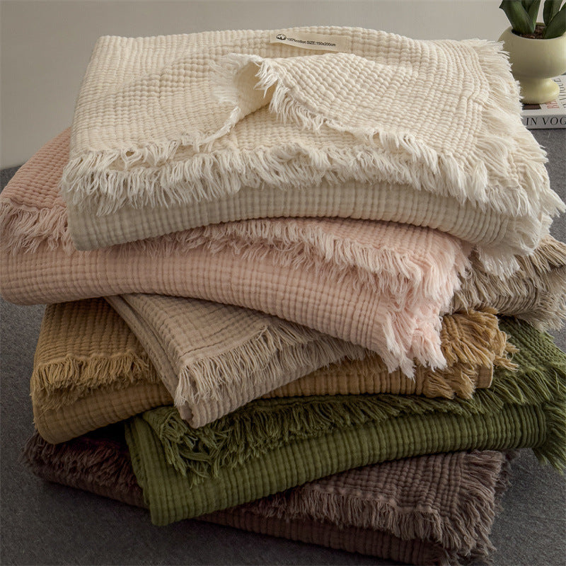 A casual, layered pile of colorful 4-layer cotton muslin throw blankets with fringe, highlighting their soft texture and comfort.