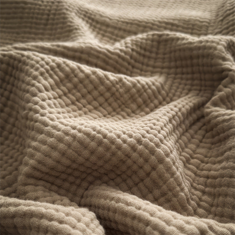 A detailed close-up shot of a beige 4-layer cotton muslin throw blanket with fringe, highlighting its soft, textured weave.