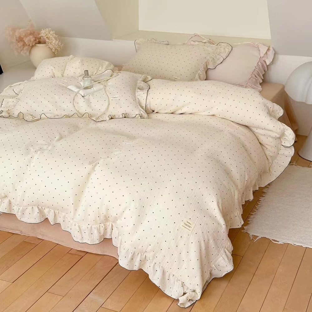 Soft polka dot bedding set with ruffled trim in white cotton gauze, styled on peach-toned bed