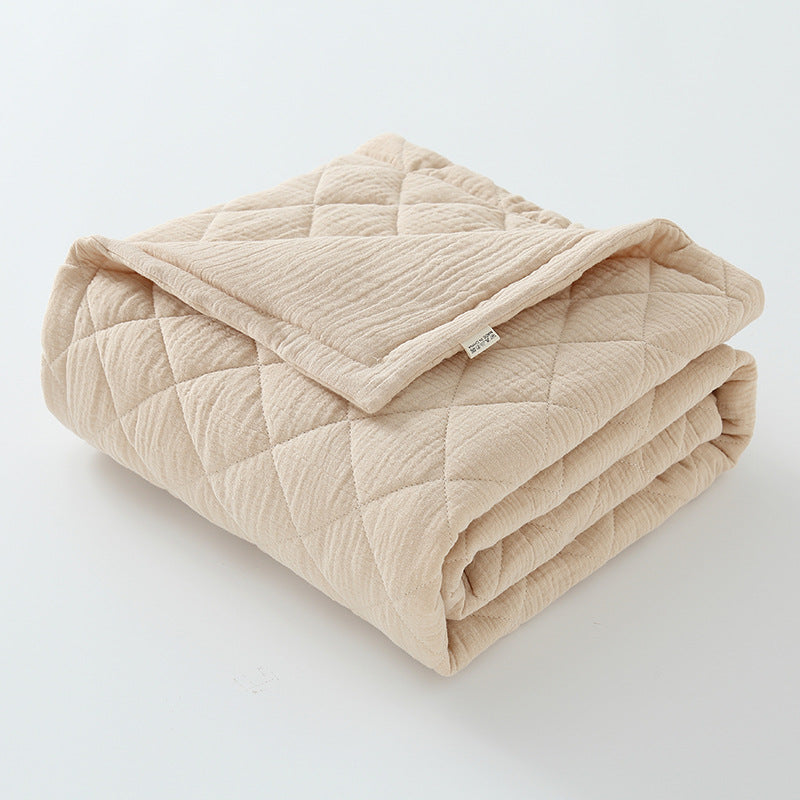 Lightweight cotton muslin quilt in khaki color folded on baby bed