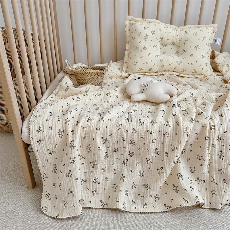 A toddler crib styled with an Olive Green Floral Muslin Blanket and Pillow Set, featuring a stuffed animal and a small woven basket.