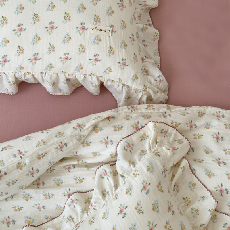 Close-up of Azalea floral cotton muslin pillowcase and ruffled duvet cover on a dusty pink crinkled cotton flat sheet