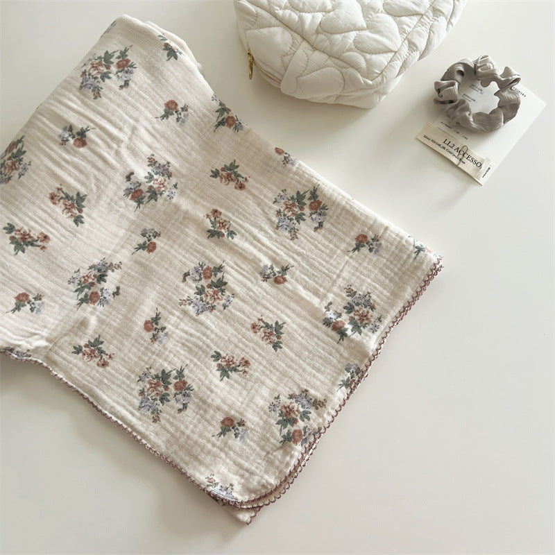A close-up, top-down view of the Vintage Floral muslin blanket, folded on a table with a quilted bag and scrunchie, highlighting the multi-colored floral clusters.