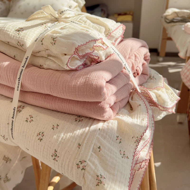 Folded small pink floral bedding set made from cotton muslin, tied with a decorative ribbon and showing the soft pink and off-white fabrics
