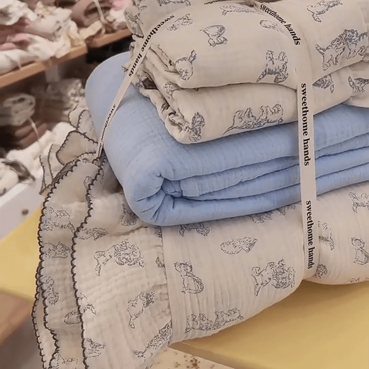 A neatly folded stack of cotton gauze duvet cover set with a blue cat print and ruffles, tied with a ribbon.