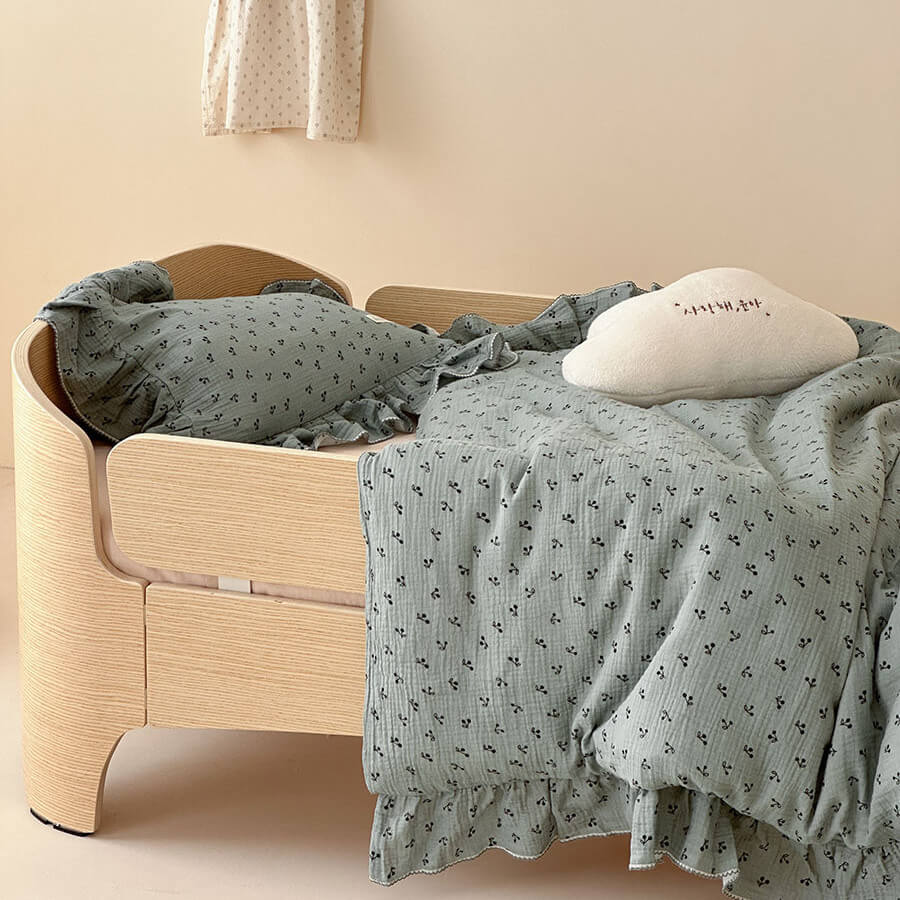 Girls' bedding set in a modern wooden toddler bed, featuring a sage ruffled duvet cover and pillow shams, with a cloud-shaped throw pillow.
