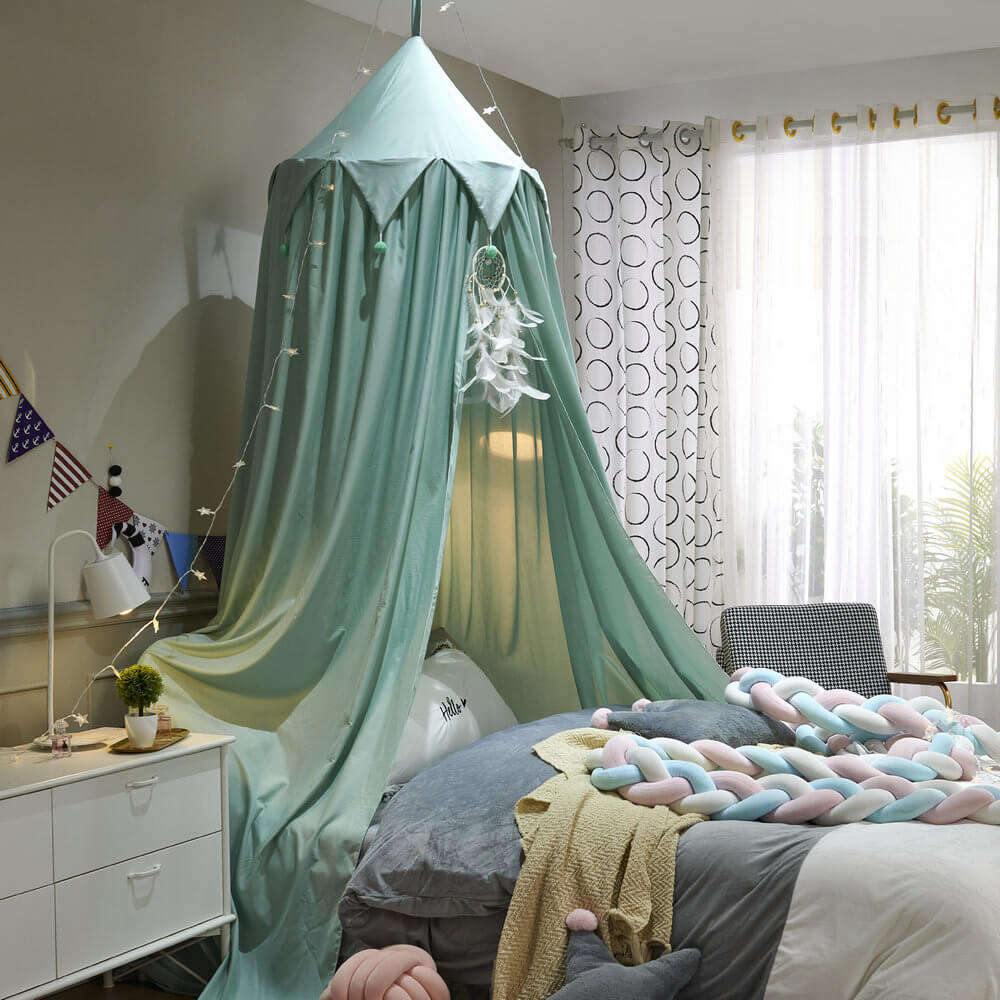 Mint green kids bed canopy with falbala ruffles and pom-poms, styled with star lights and a dreamcatcher for a cozy room.