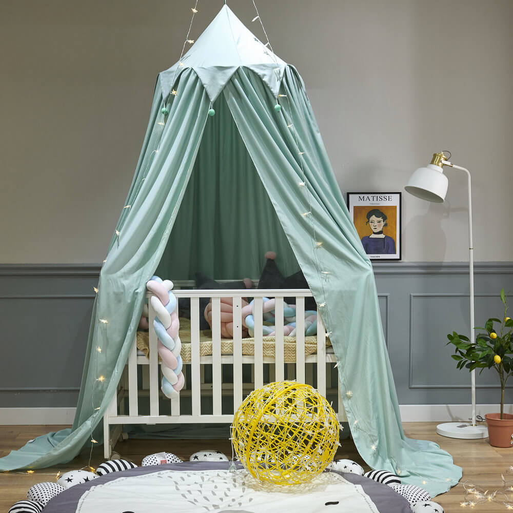 Mint green kids bed canopy with falbala ruffles and pom-poms, set up over a baby crib to create a beautiful nursery.