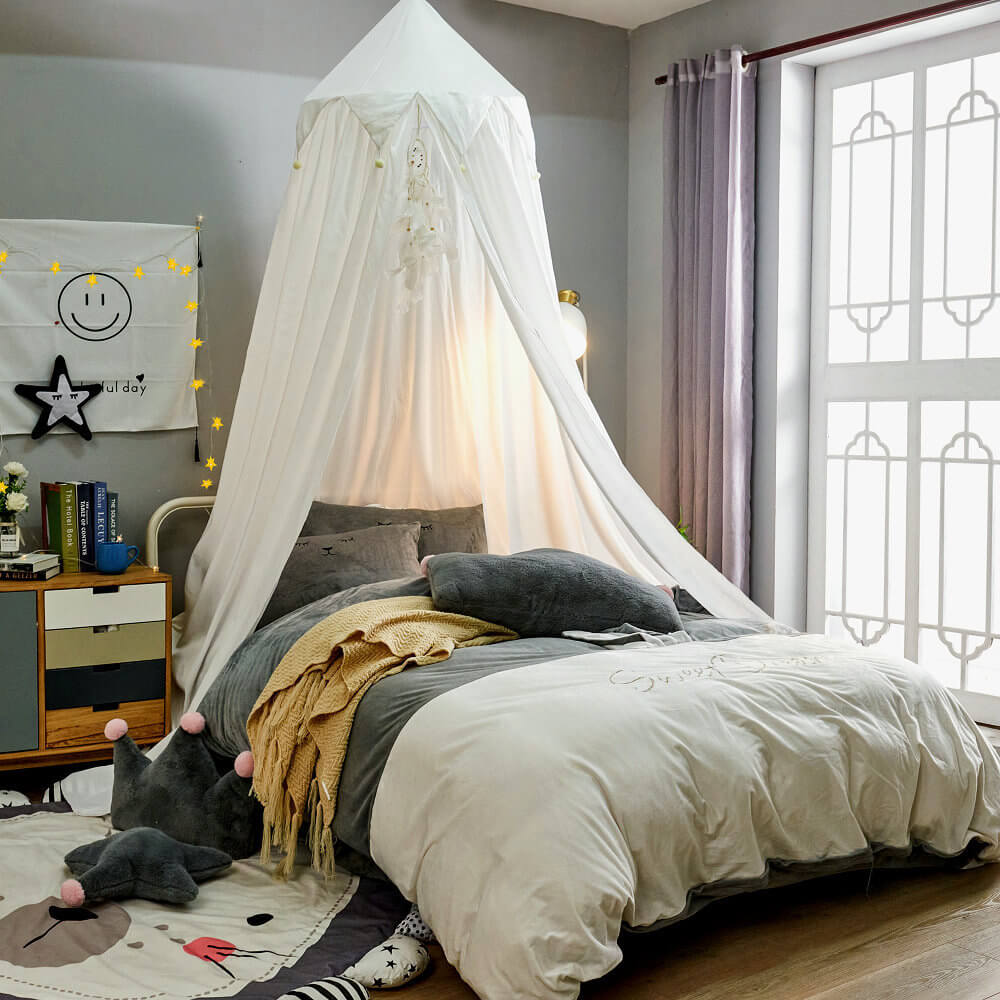 White kids bed canopy with falbala ruffles and pom-poms, installed over a bed with gray bedding and a star-themed room decor.