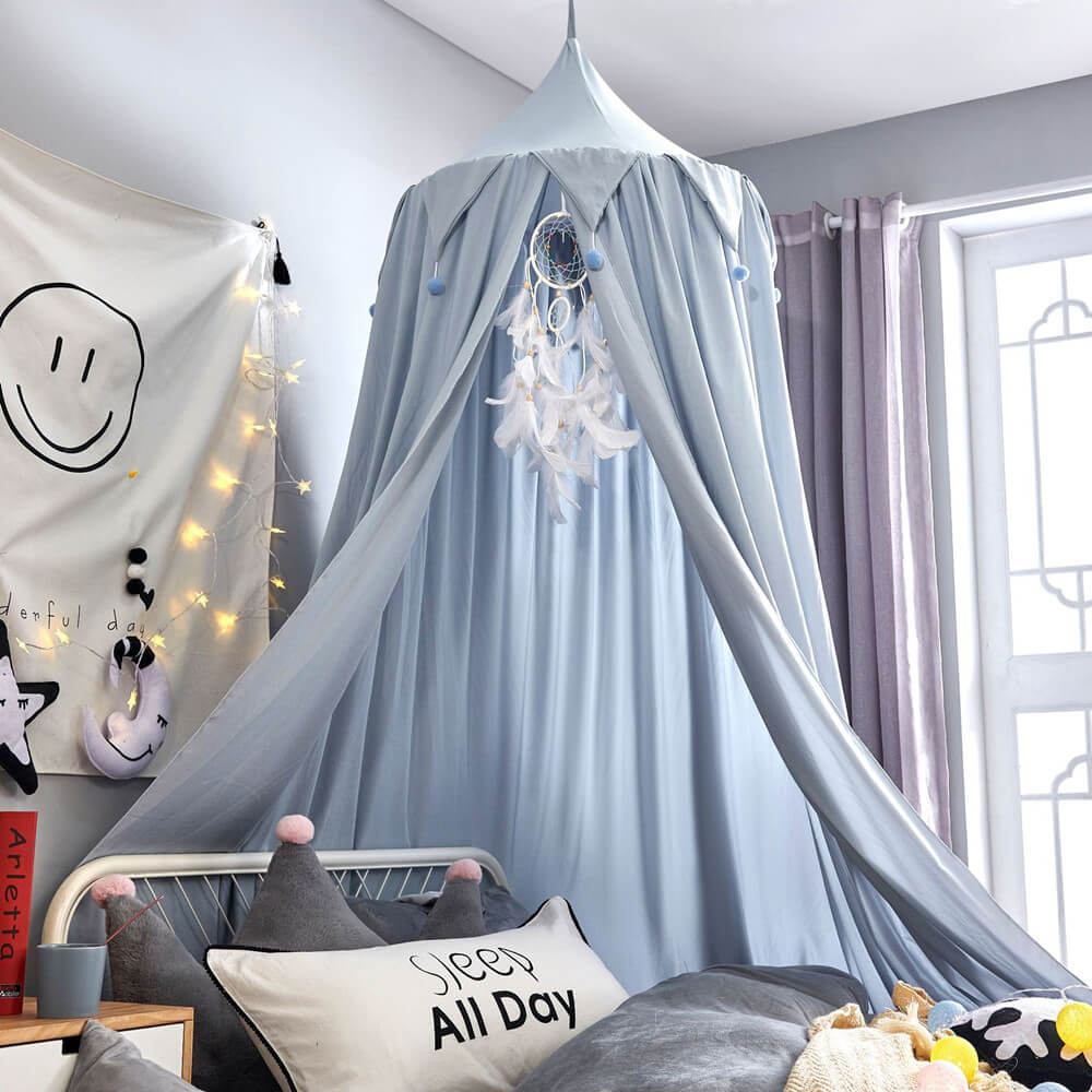 Light blue kids bed canopy with falbala ruffles and pom-poms, decorated with string lights and a dreamcatcher for a serene bedroom.