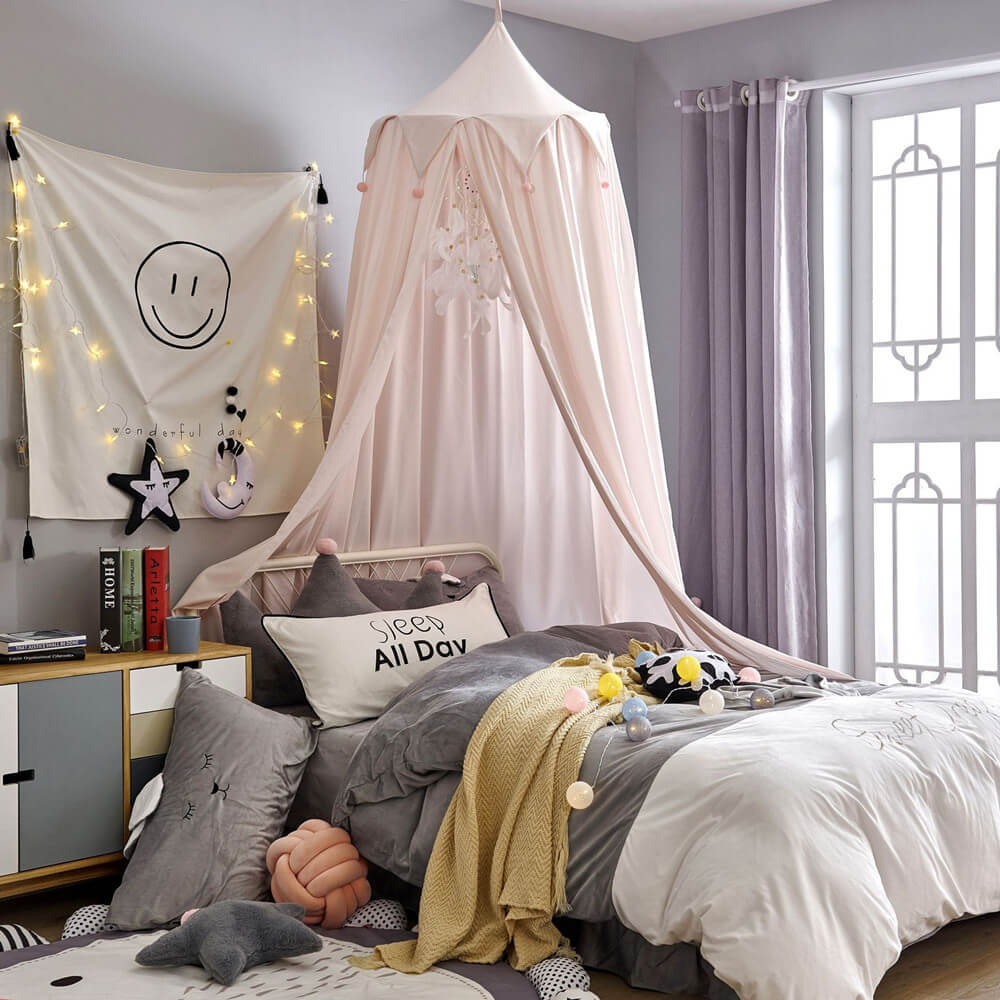 Blush pink kids bed canopy with falbala ruffles and pink pom-poms, styled as an elegant centerpiece for a child's bed.
