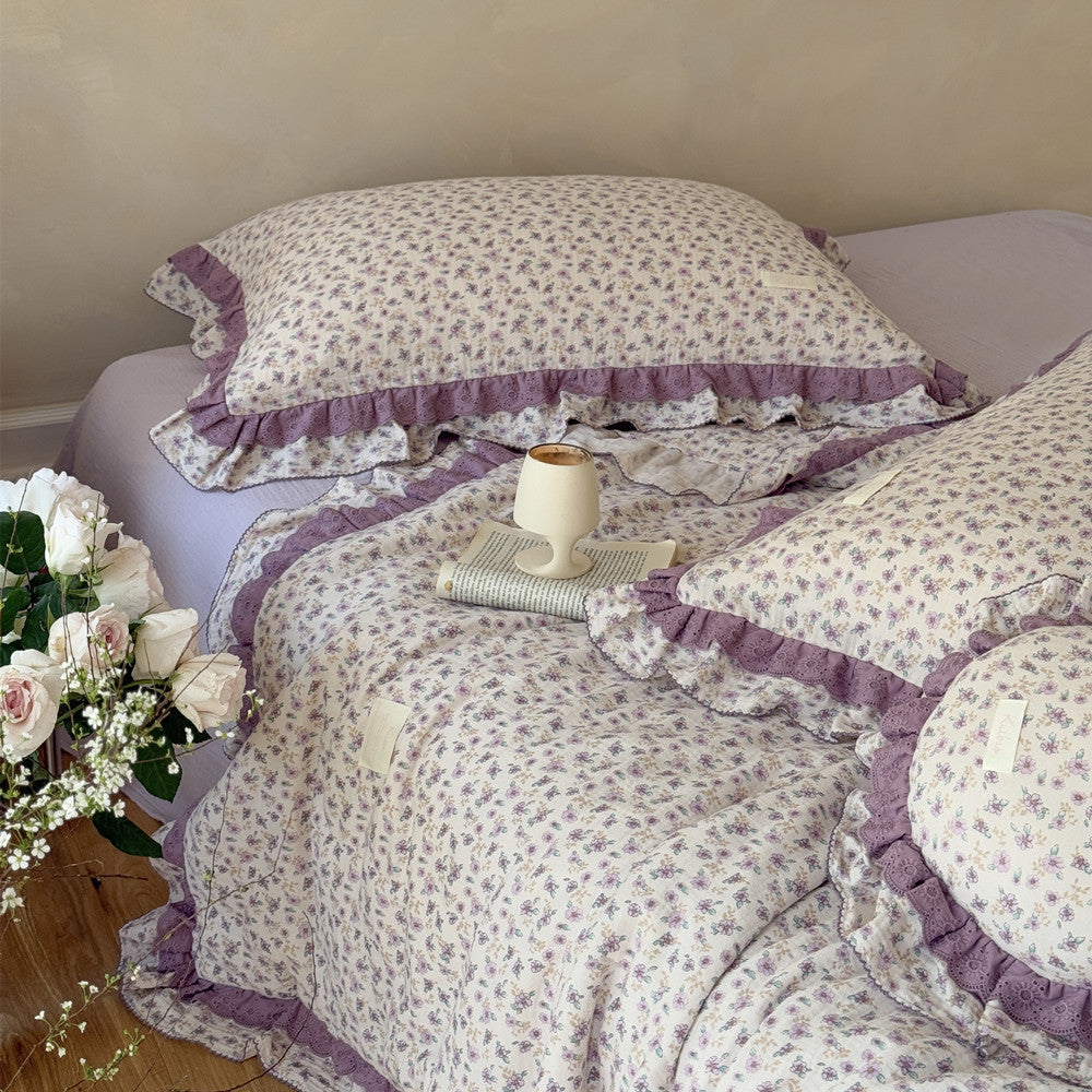 Lavender floral comforter on wood floor, paired with soft white roses