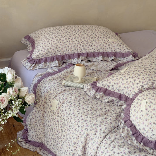 Lavender floral comforter on wood floor, paired with soft white roses
