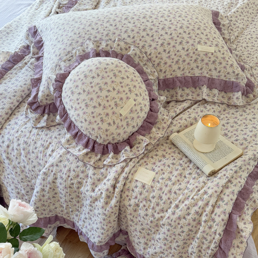 Side view of lavender floral comforter and bouquet in softly lit bedroom