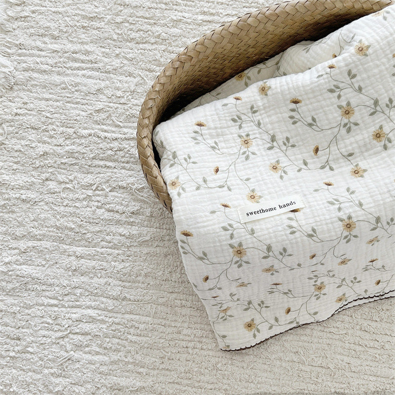 Yellow floral cotton muslin baby blanket folded neatly in a woven basket with the product label visible.