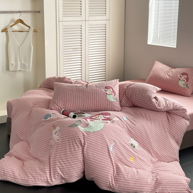 Pink striped bedding set with mermaid design on a bed in a room.