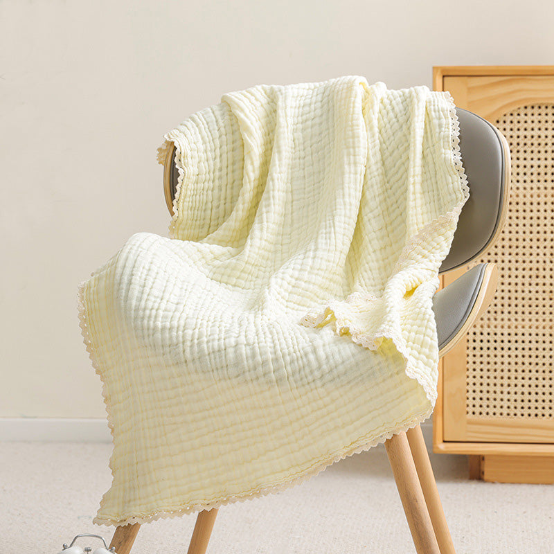 A buttery yellow 6-layer muslin baby quilt with a decorative lace trim draped over a gray chair.