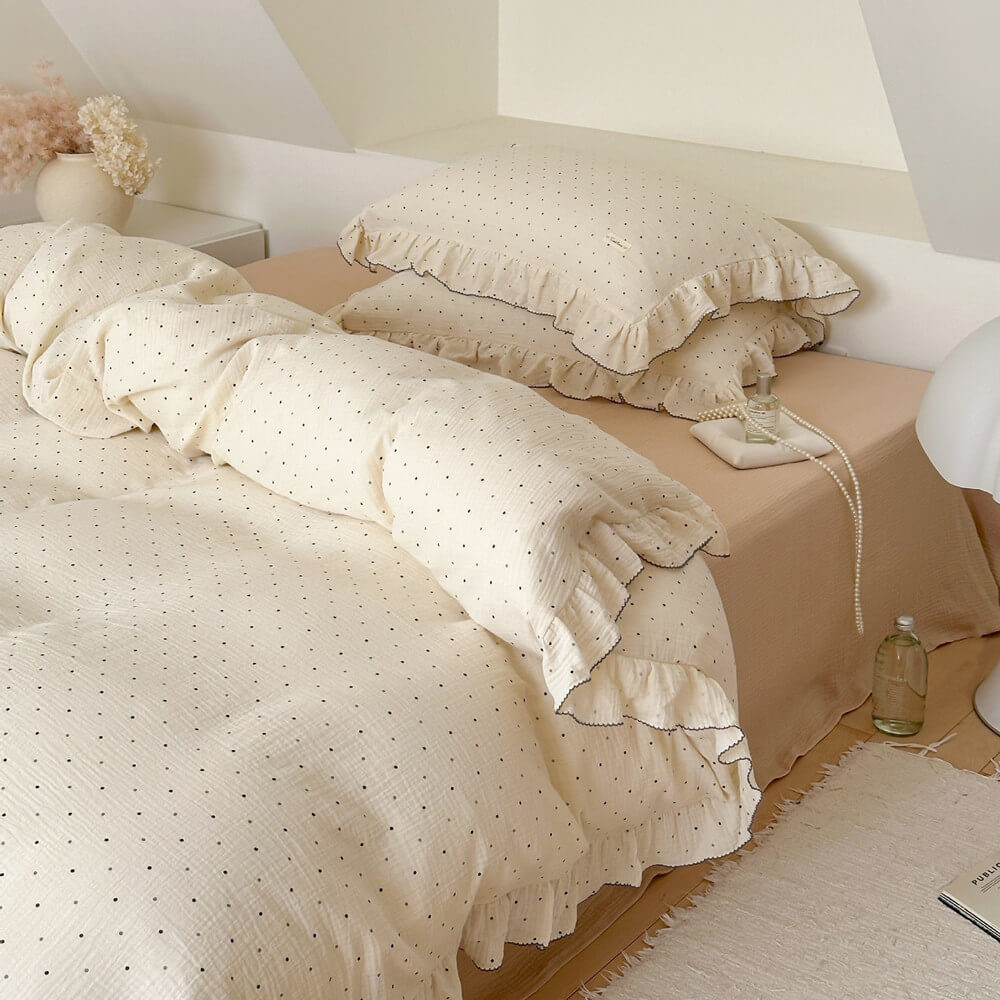 Layered ruffled pillowcases in polka dot cotton gauze with soft blush underlayer, styled on neutral twin bedding