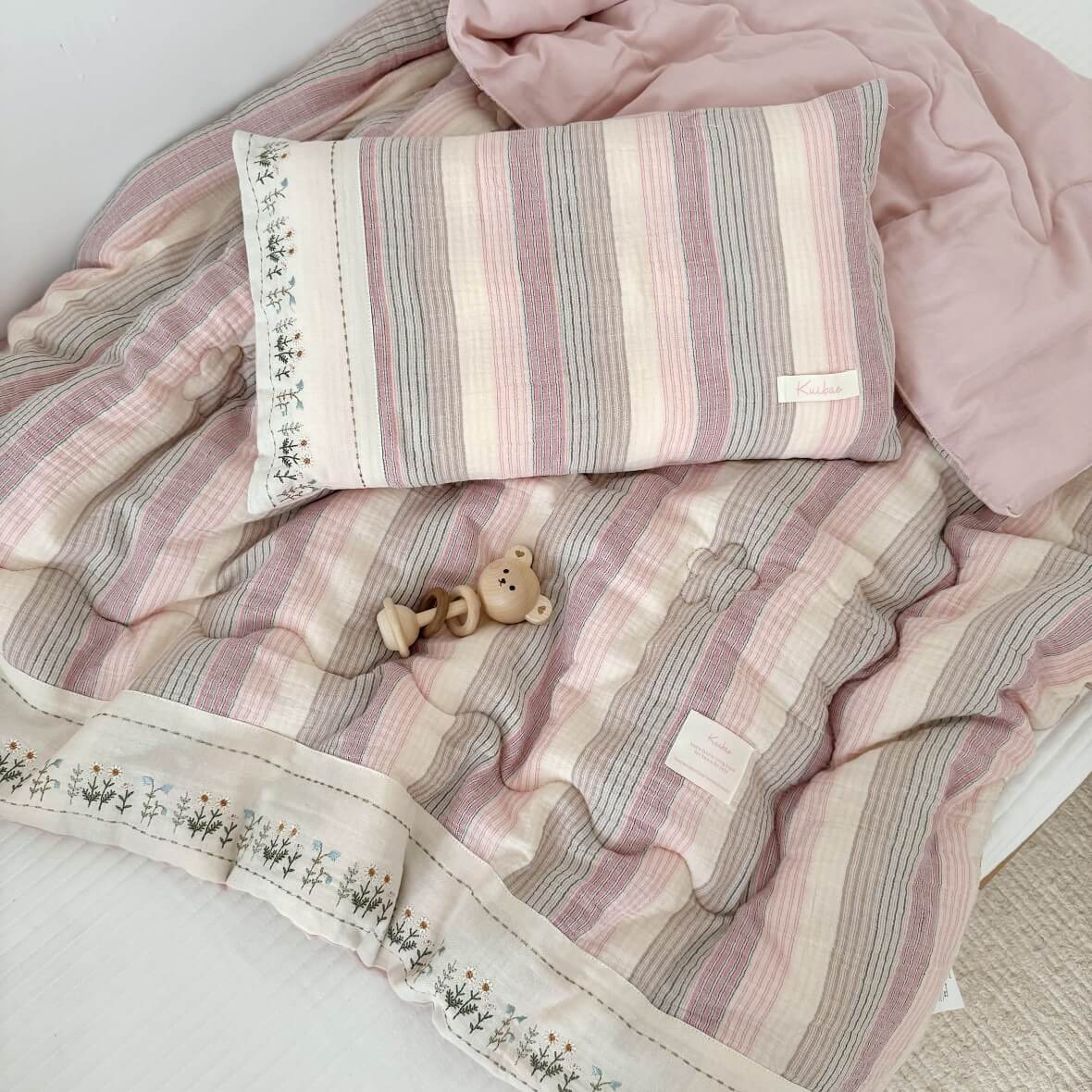 Soft pink striped cotton comforter set and matching pillowcase on a bed, showing the light pink solid reverse side