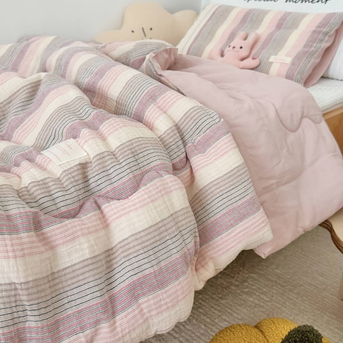 Pink and gray striped comforter on a bed with plush toys.