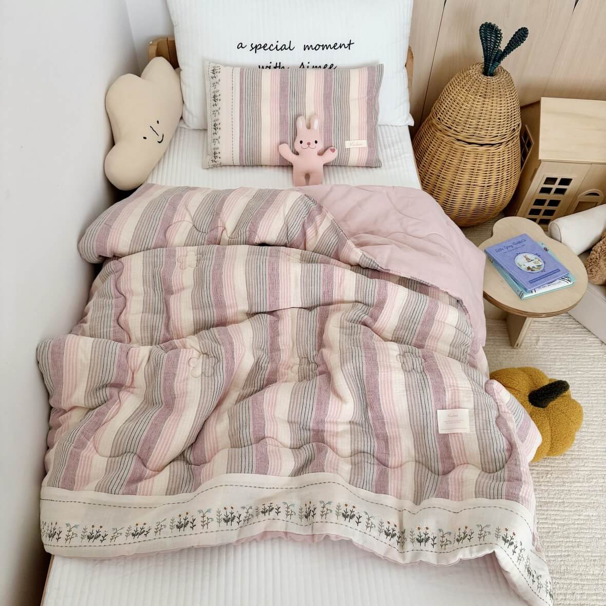Striped pink and white comforter on a bed with decorative pillows and a teddy bear.
