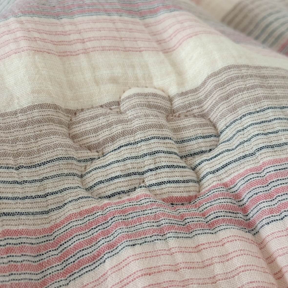 Close-up of the flower-shaped quilting detail on the soft pink striped muslin comforter