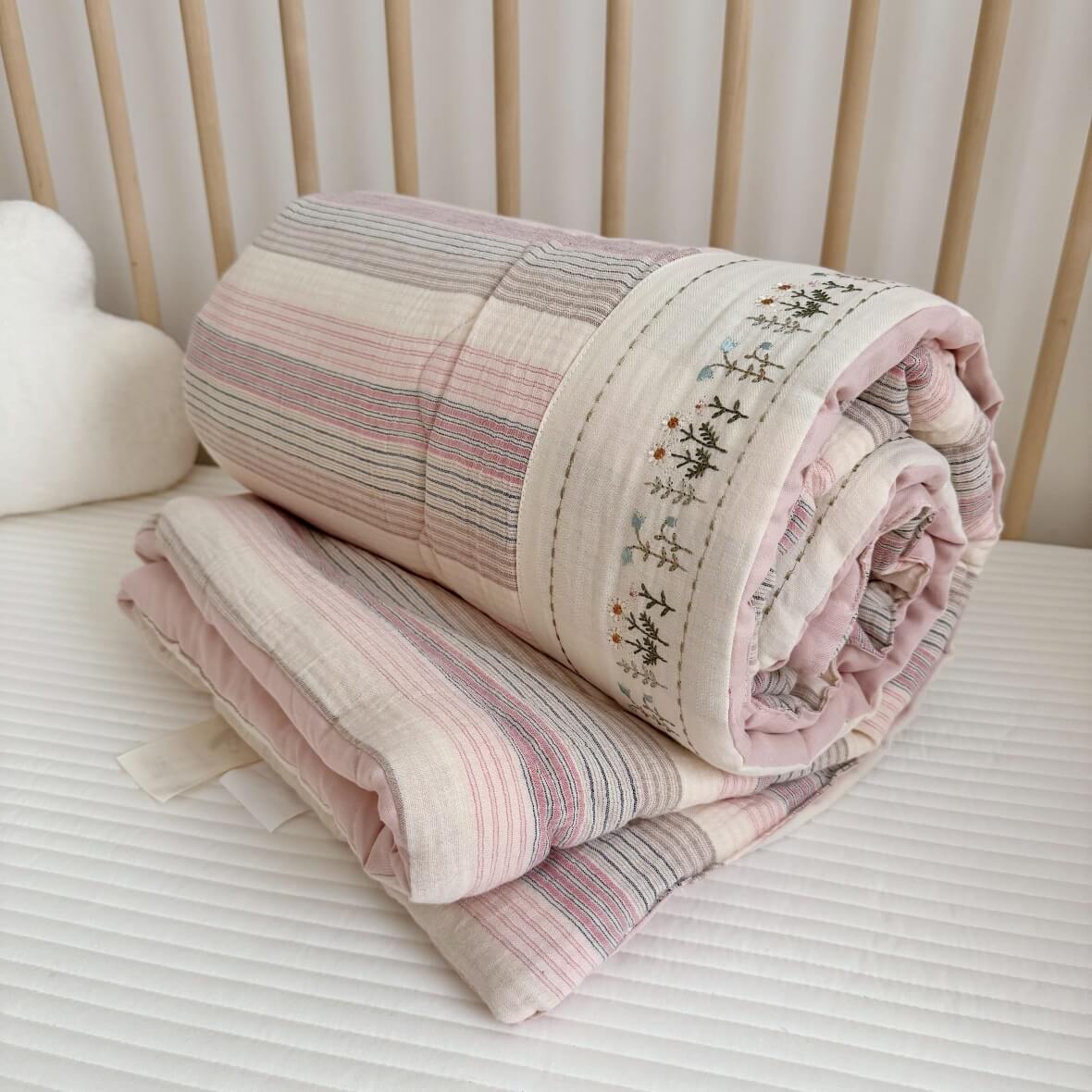 Rolled-up pink striped muslin quilt set, showing the embroidered floral border and soft texture