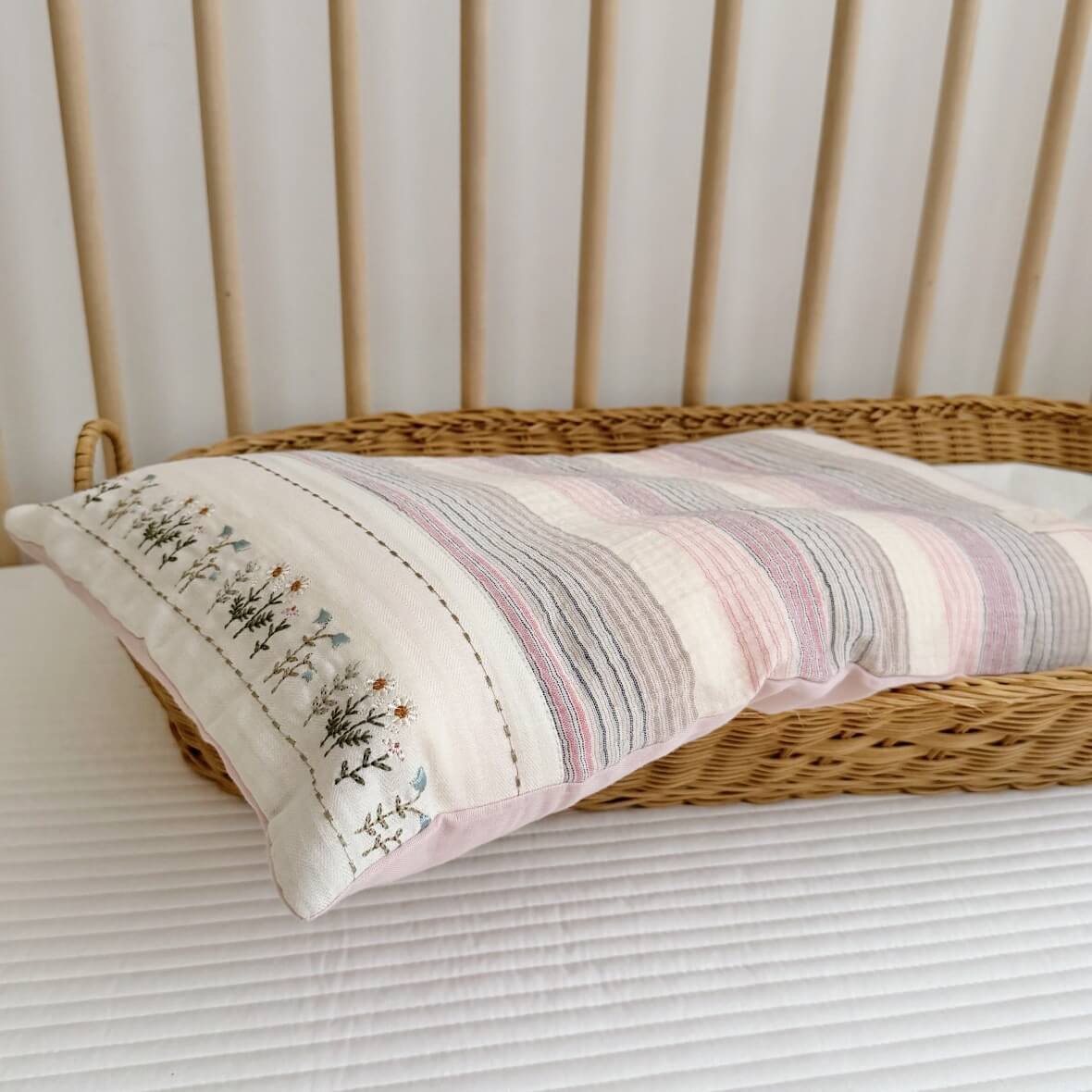 Embroidered floral border on the matching pillowcase from the pink striped muslin quilt set, placed in a rattan basket