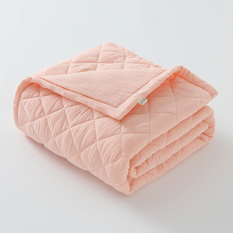 Soft peach pink cotton muslin baby quilt neatly folded with quilted texture