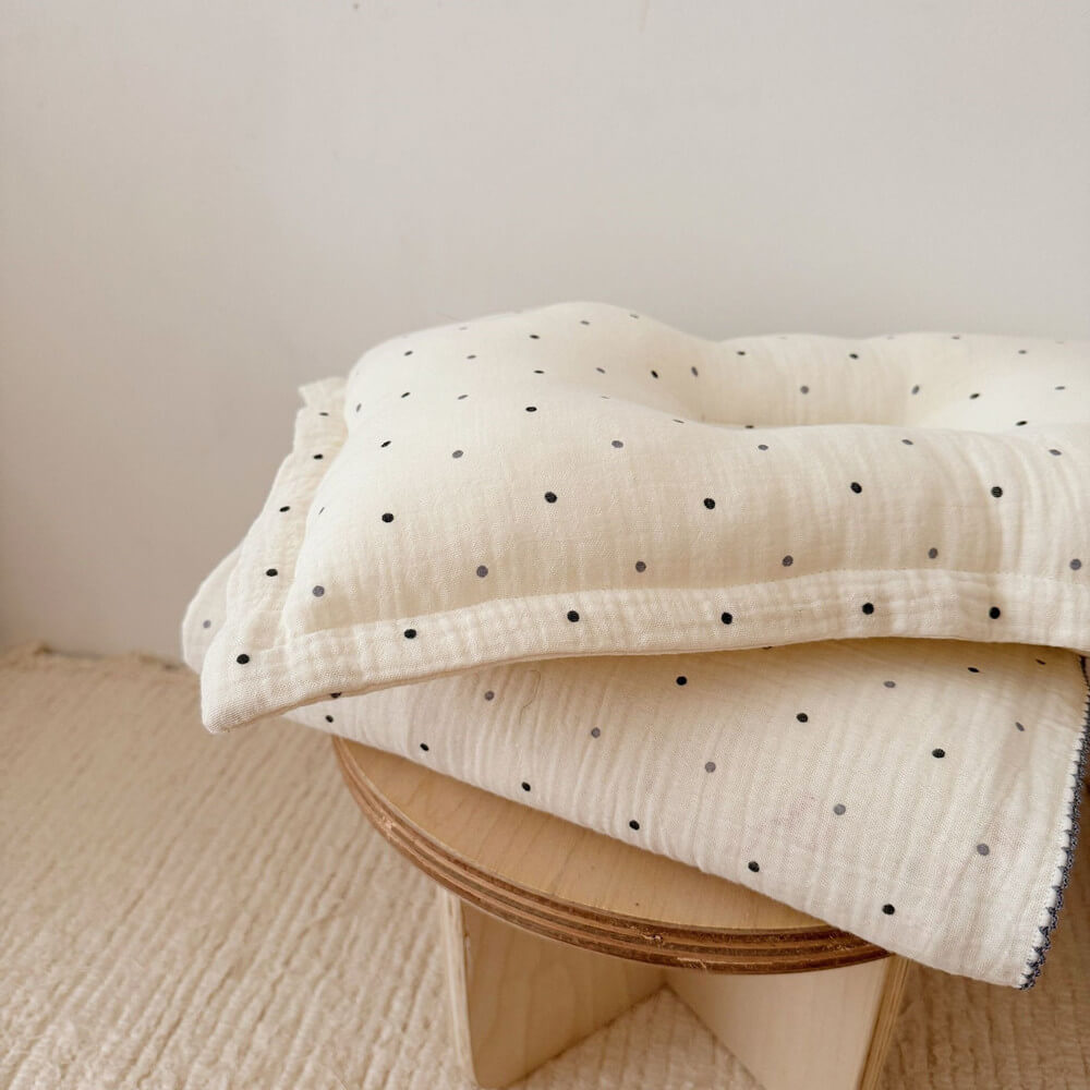 A side shot of the folded Polka Dot muslin blanket and matching pillow, highlighting the crinkled texture and the soft, scalloped edges.