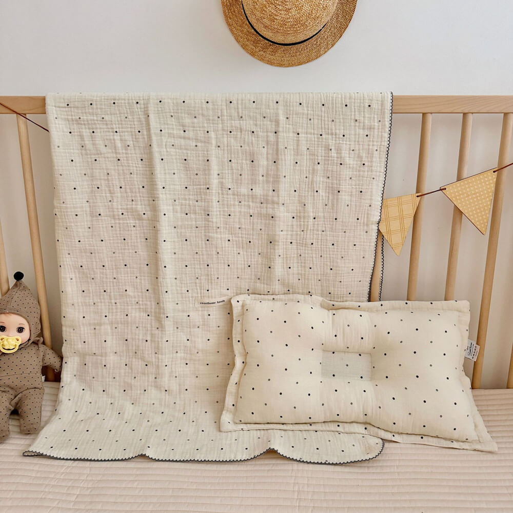 A full view of the Polka Dot muslin toddler blanket and pillow set displayed in a crib, showing the complete product on a quilted mattress with a doll.