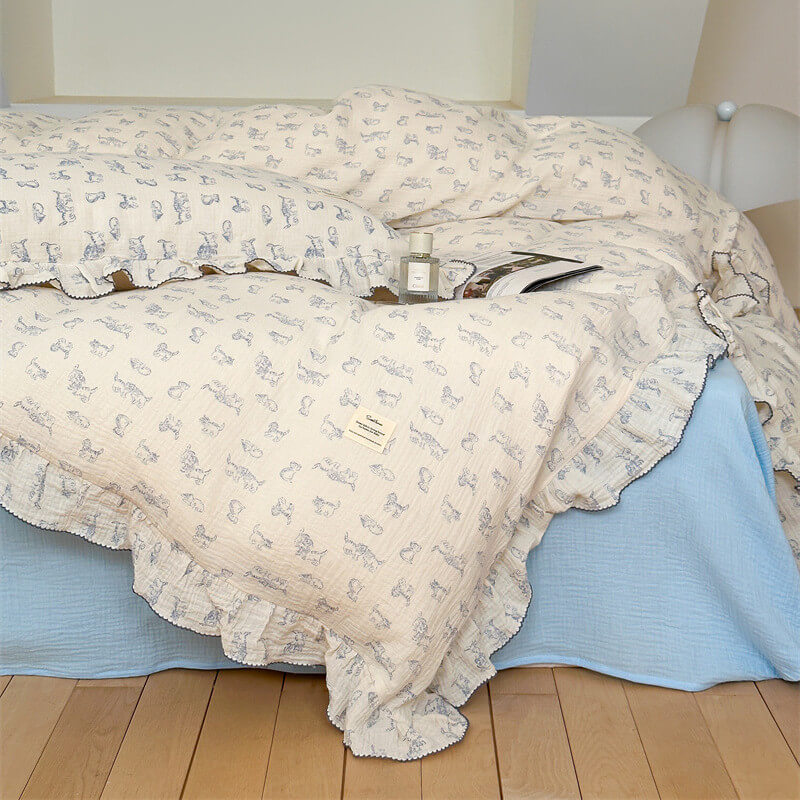 A stylish bed with a draped white cotton gauze duvet cover and matching pillow shams, featuring a subtle blue cat print and ruffled trim