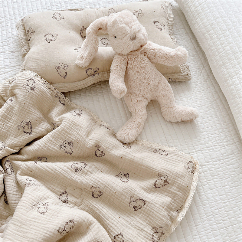 Bunny print cotton muslin comforter and pillow set displayed on white bedding with plush toy