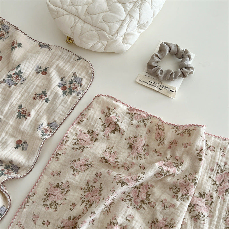 Rosebud pink floral muslin baby blanket next to a scrunchie and white quilted pouch